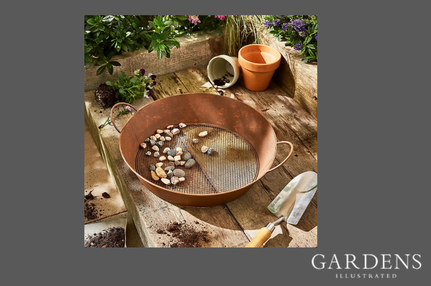 Dunelm Iron Rust Garden Sieve with pebbles in a garden