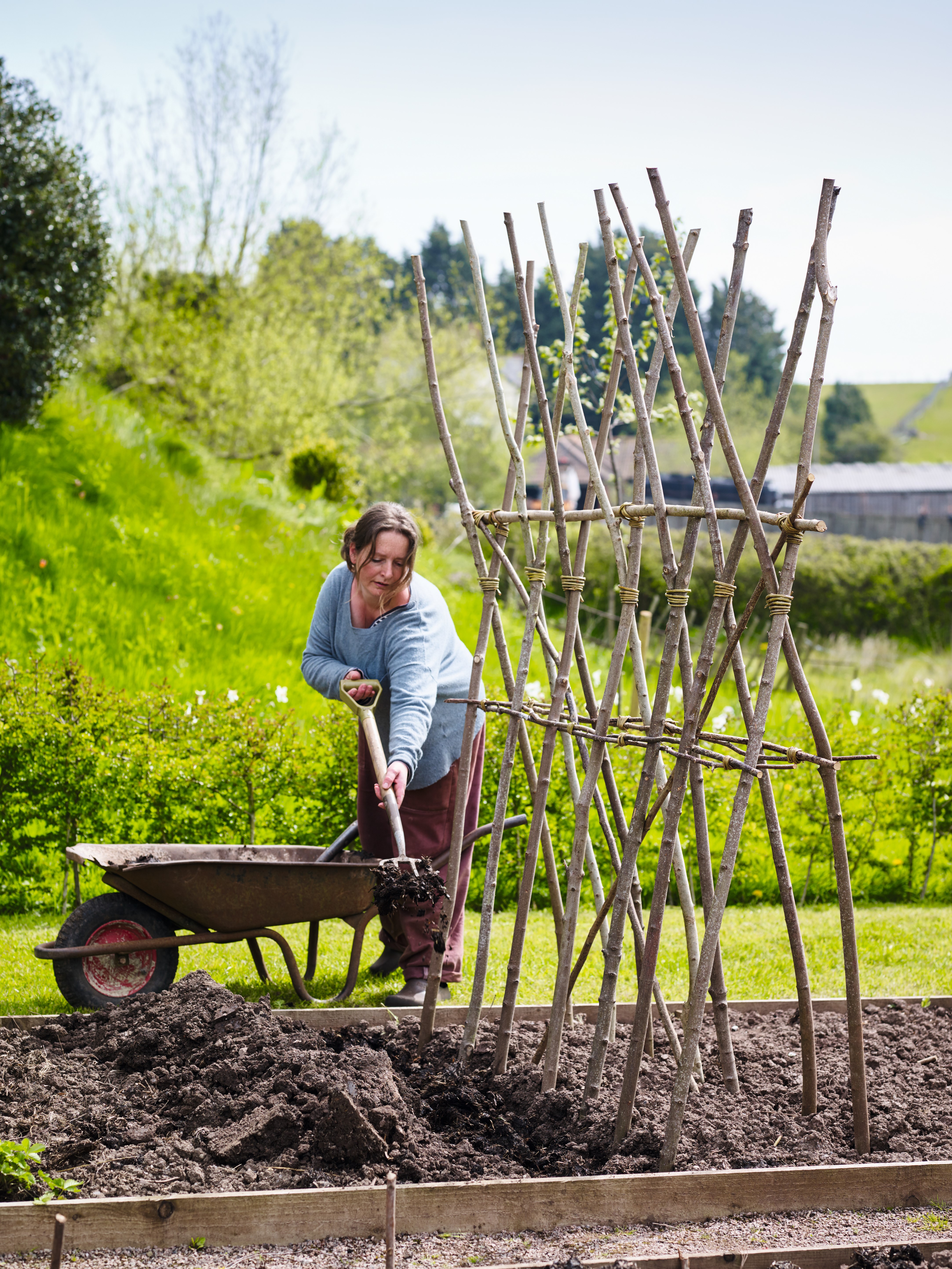 A woman gardening in a vegetable garden with plant supports 